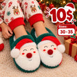 Child in reindeer print pyjamas wearing green plush slippers with smiling Santa faces and red hats
