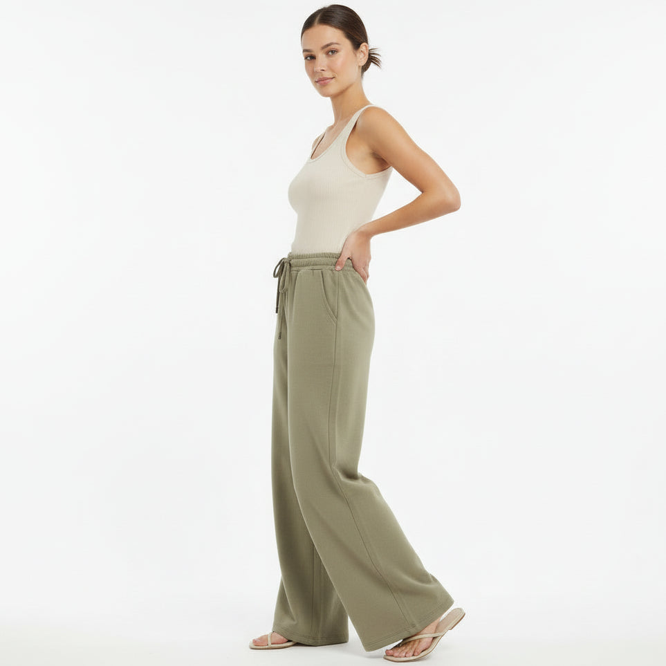 Woman wearing a white tank top and olive green wide-leg pants on a white background