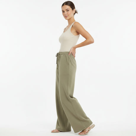 Woman wearing a white tank top and olive green wide-leg pants on a white background