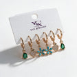 Three pairs of gold huggies with green teardrop, pave heart and turquoise daisy drops on a card