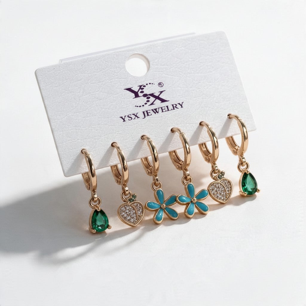Three pairs of gold huggies with green teardrop, pave heart and turquoise daisy drops on a card