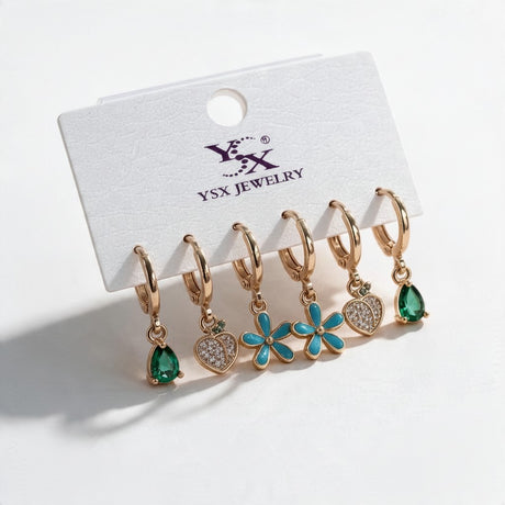 Three pairs of gold huggies with green teardrop, pave heart and turquoise daisy drops on a card
