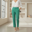 Woman wearing a white blouse and green trousers in a minimalistic room