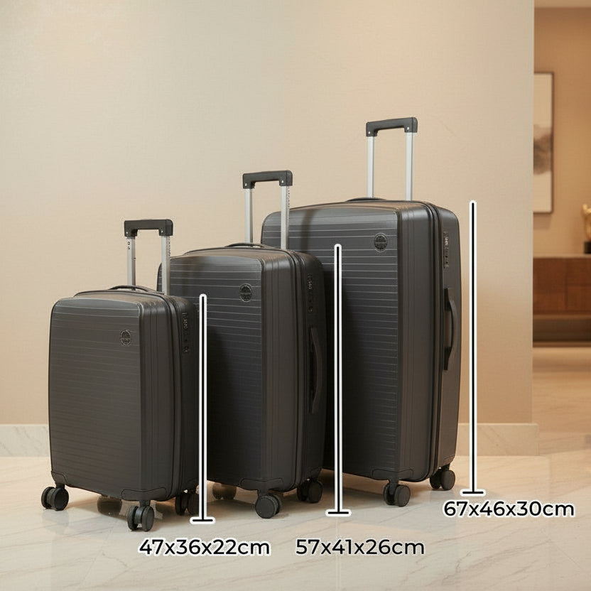 Three dark grey suitcases lined up by size against a warm beige wall