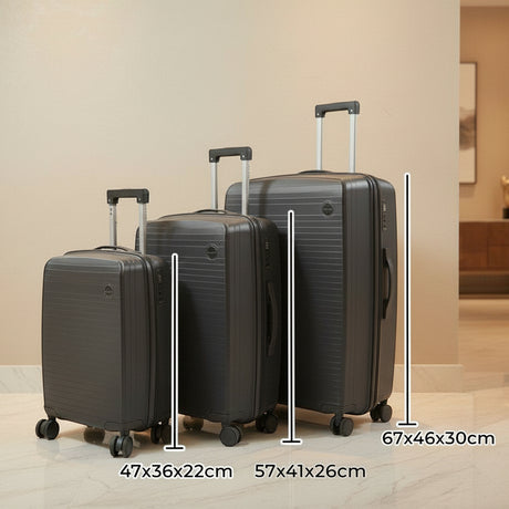 Three dark grey suitcases lined up by size against a warm beige wall