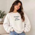 Woman in a grey sweatshirt with an All Money Back My Home slogan print and light blue jeans