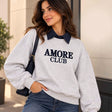 Woman in a heather grey Amore Club sweatshirt with navy embroidery over a navy collared shirt