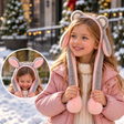 Girl in a pink puffer wearing a grey plush ear headband with long floppy ears and pink pom poms