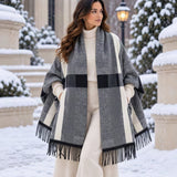 Light grey block check blanket wrap with cream stripes and black fringe worn over a cream outfit in the snow
