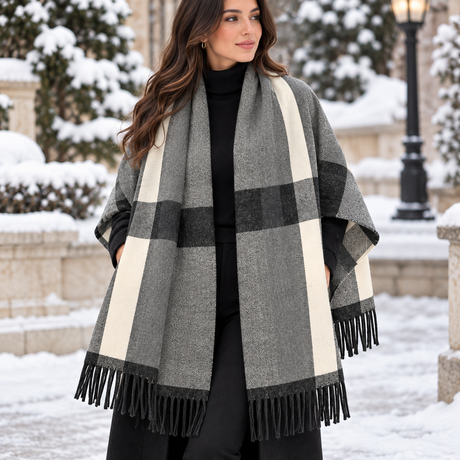 Woman in a snowy street wearing a grey herringbone blanket wrap with cream and black block check and black fringe
