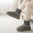 Grey suede look ankle boots with white zigzag embroidery, worn in a bright white room