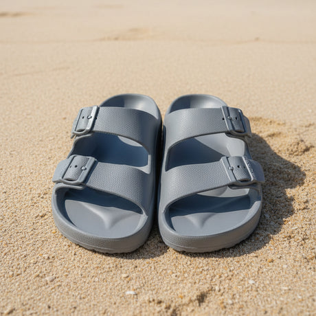 Pair of grey buckle slides on a sandy surface