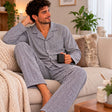 Man on a sofa with a mug wearing a grey herringbone button front pyjama shirt and trousers