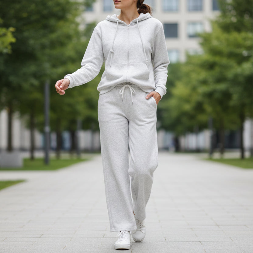 Person wearing a grey casual outfit walking on a sidewalk with trees and buildings in the background