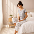 Woman sitting on a bed in a grey cat print pyjama top and cropped trousers