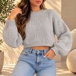 Woman in a light grey chunky ribbed knit cropped sweater with balloon sleeves and blue jeans