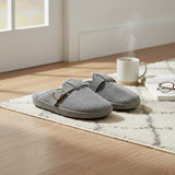 Pair of grey corduroy buckle slippers resting on a patterned rug by a mug