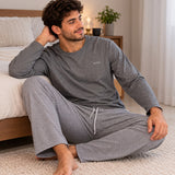Man sitting on a bedroom rug in a charcoal long sleeve top and checked drawstring trousers