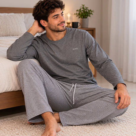 Man sitting on a bedroom rug in a charcoal long sleeve top and checked drawstring trousers