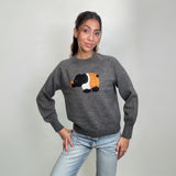 Grey knit sweater with a fuzzy black, white and orange elephant patch, hands on hips