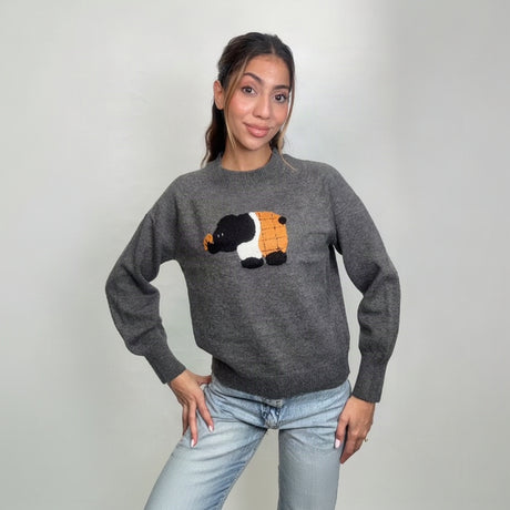 Grey knit sweater with a fuzzy black, white and orange elephant patch, hands on hips
