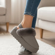 Grey slippers with fuzzy trim worn indoors on a carpeted floor.