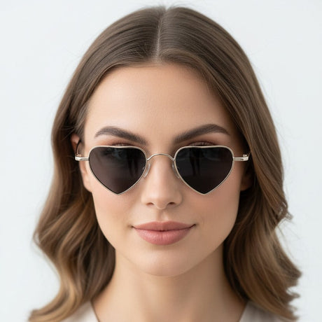 Grey heart-shaped sunglasses worn by a model with a plain background