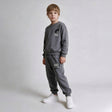 Boy in a grey crew neck sweatshirt and drawstring joggers with white sneakers