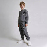 Boy in a grey crew neck sweatshirt and drawstring joggers with white sneakers