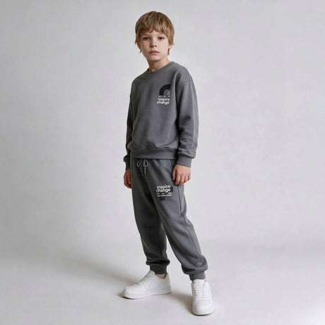 Boy in a grey crew neck sweatshirt and drawstring joggers with white sneakers