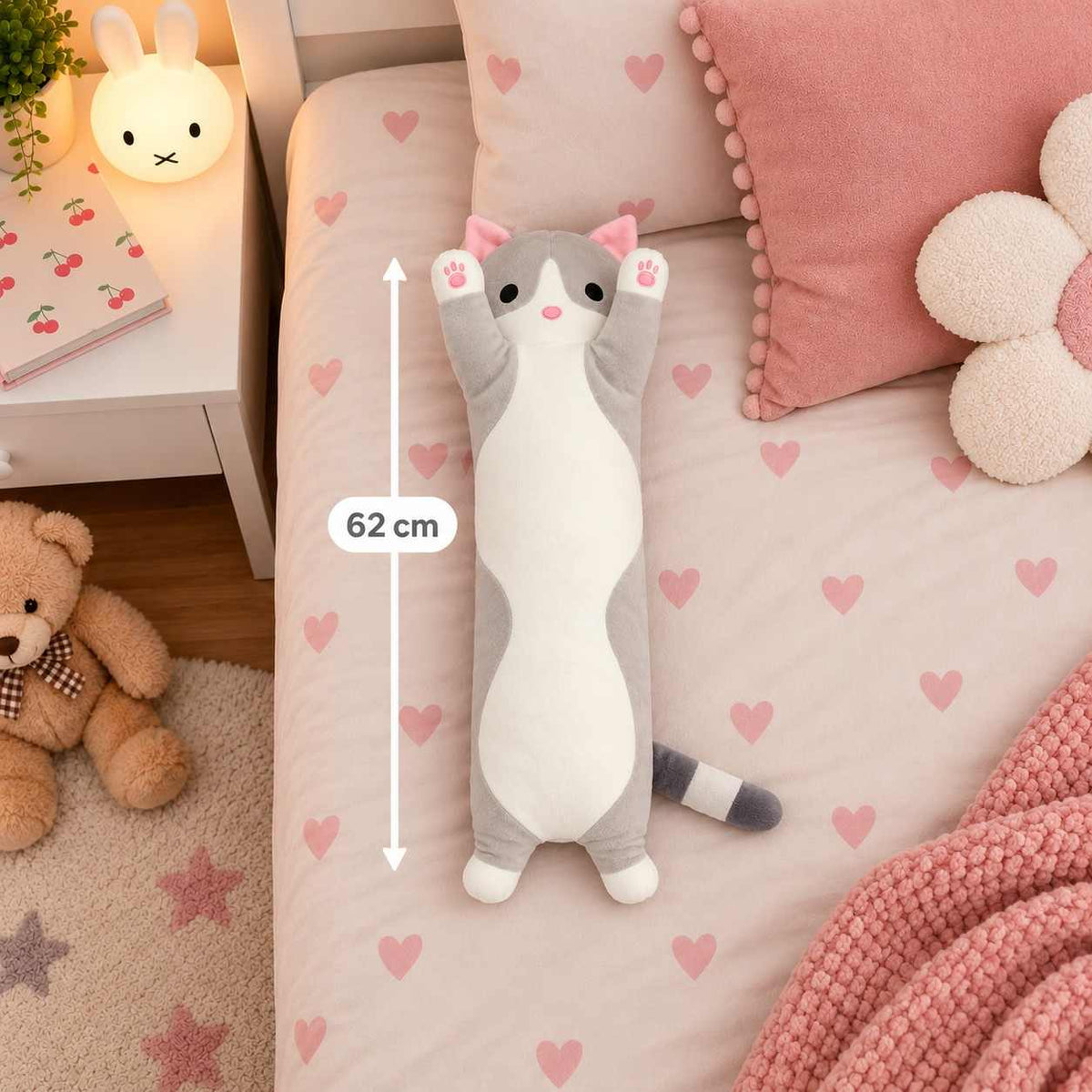 Grey long cat body pillow plush lying on a heart print bed next to a 62 cm measuring line