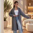 Grey long fuzzy knit coat worn open over a white crop top and jeans, one arm stretched out