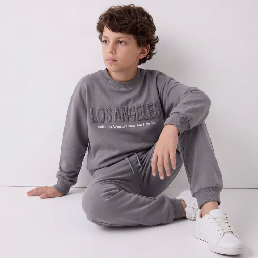 Boy sitting on the floor in a grey Los Angeles sweatshirt jogging set