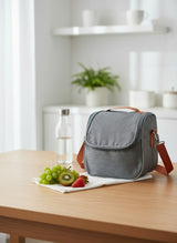 Grey lunch box on a wooden table with fruits and a bottle