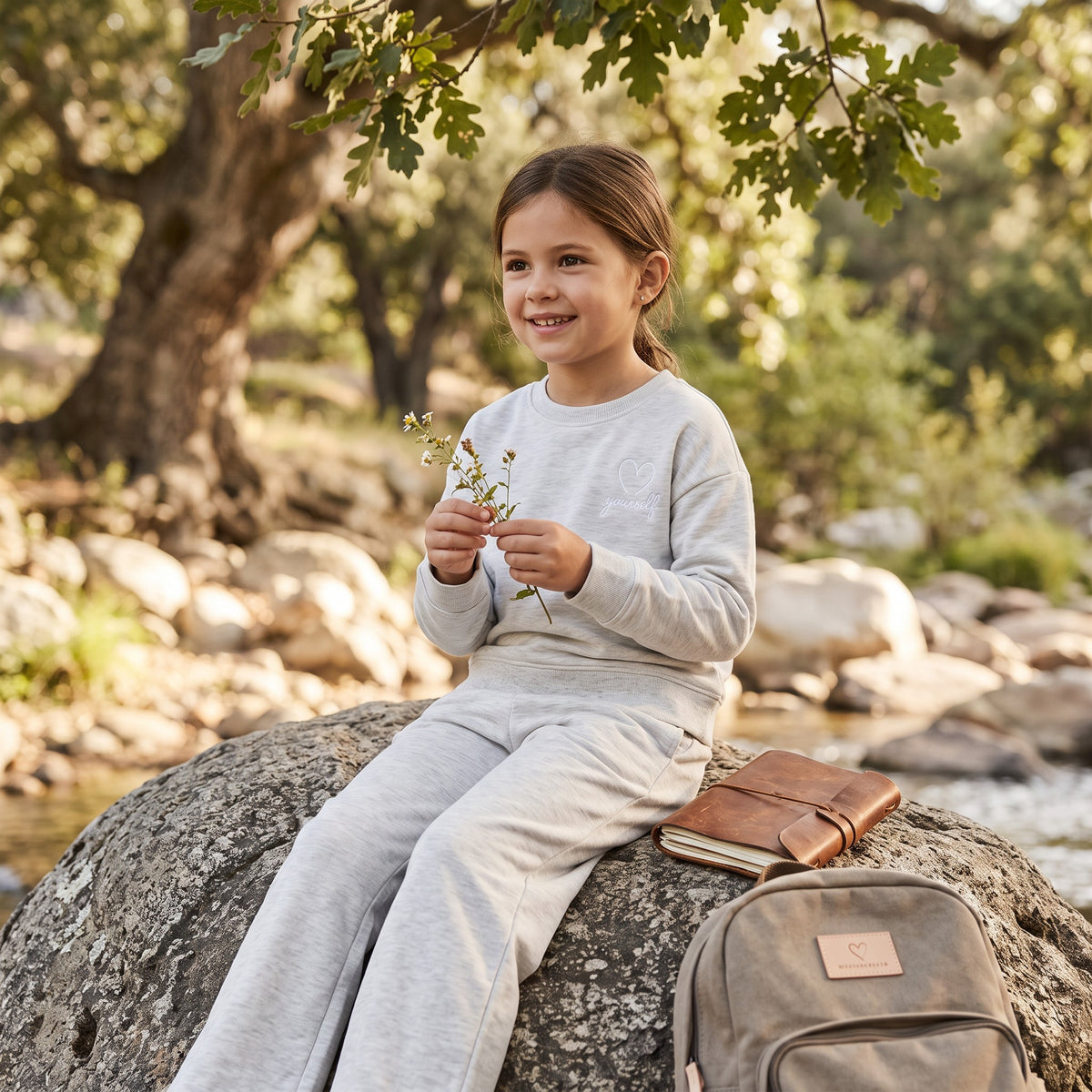 Girl holding wildflowers on a riverside rock in a heather grey sweatshirt and matching sweatpants