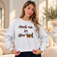 Woman with sunglasses on her head in a heather grey Meet me in New York sweatshirt with brown lettering