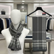 Grey plaid scarf on a mannequin and hanger in a store setting