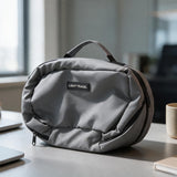 Grey padded travel pouch with a carry handle and Light Travel patch on a desk