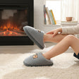 Child wearing grey ribbed kids slippers with a bear patch and fleece lining by a fireplace
