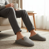 Grey ribbed slippers worn in an armchair with a warm drink on a soft carpet
