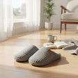 Pair of grey ribbed slippers on a wood floor beside an open book and a mug