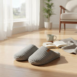 Pair of grey ribbed slippers on a wood floor beside an open book and a mug