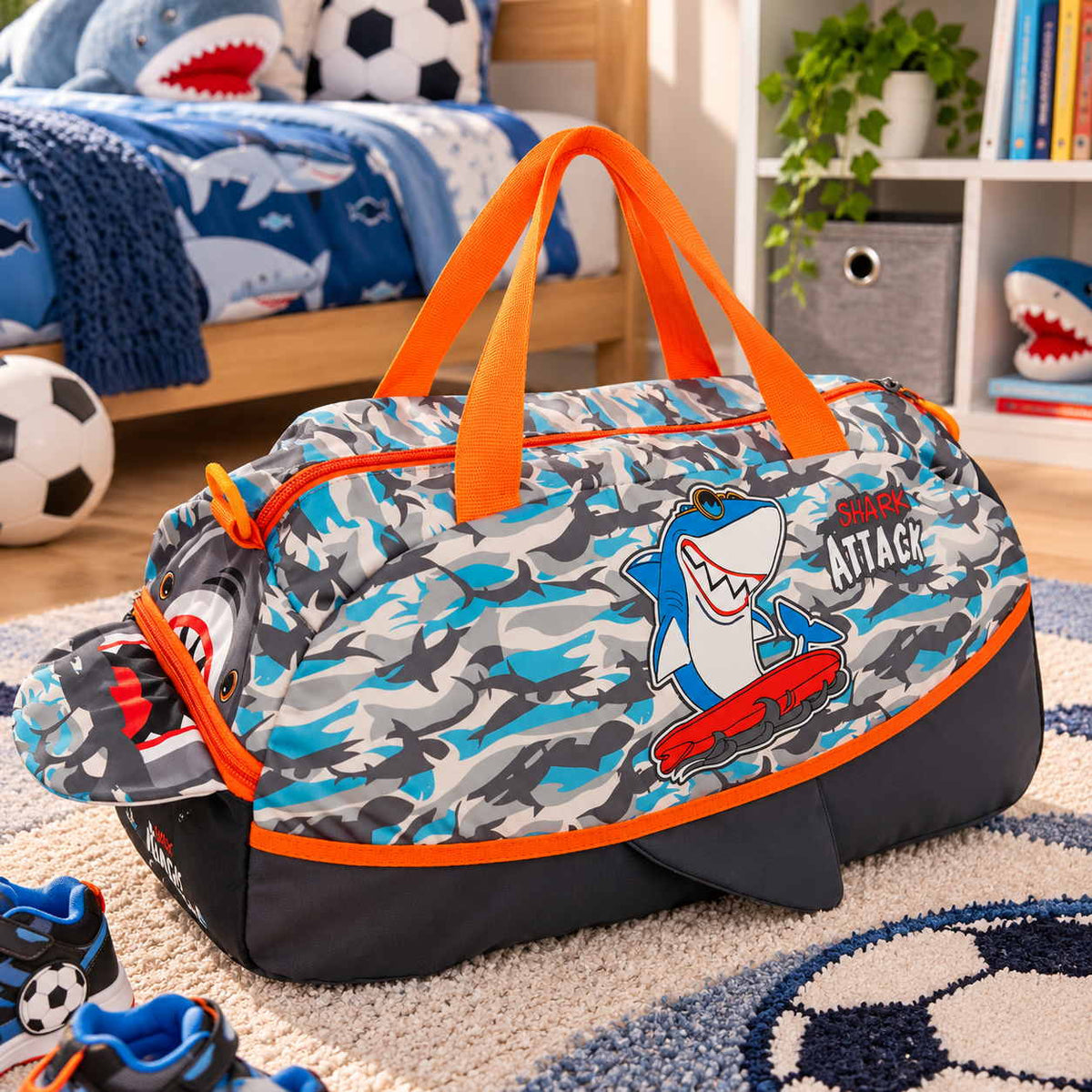 Grey and blue shark camo duffle bag with orange handles, a shark mouth end and a skateboarding shark