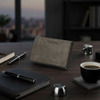 Gray wallet on a wooden desk with a notebook, pen, and coffee cup.