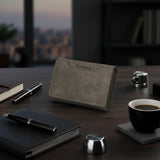 Gray wallet on a wooden desk with a notebook, pen, and coffee cup.