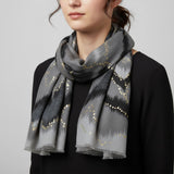 Person wearing a grey scarf with gold patterns on a plain background