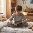 Boy in a grey and white striped pajama set reading on the bed