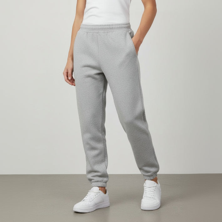 Person wearing grey sweatpants and white sneakers on a plain background
