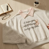 Close view of pink teddy bear embroidery and cursive slogan on grey marl fleece