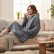 Grey fleece hooded blanket with teddy bear embroidery worn relaxing on a sofa with a warm drink